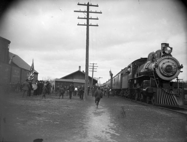 Crowd of people and a band meet a train, possibly troops leaving for World War I.