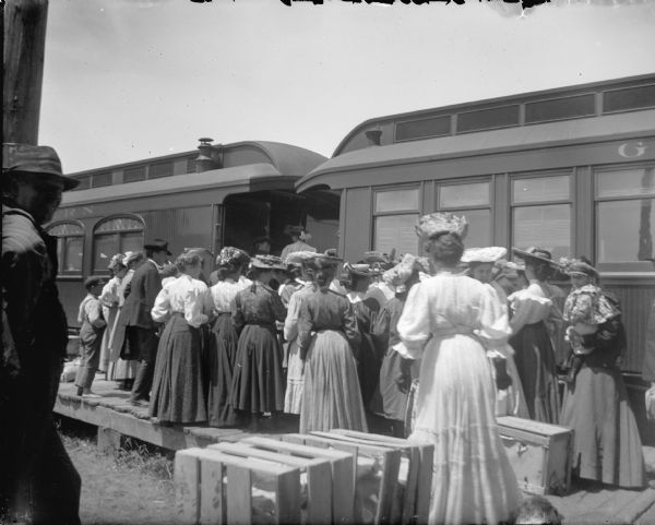A group of women, probably wearing their best dresses and hats, meeting a Green Bay & Western train. The photograph was probably taken near Black River Falls.