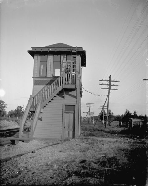 Man standing on the top of the stairway of the railroad switch control tower, probably just outside Sheppard, Wisconsin.