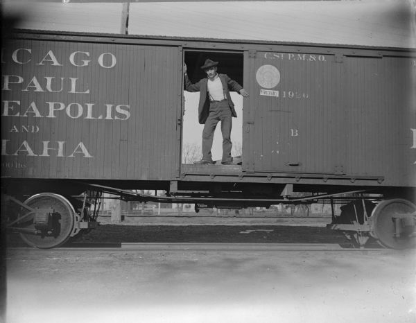 A man stands in the open doorway of a Chicago, St. Paul, Minneapolis, & Omaha railway boxcar.
