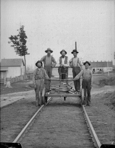 Railroad workers posing with a handcar on railroad tracks.