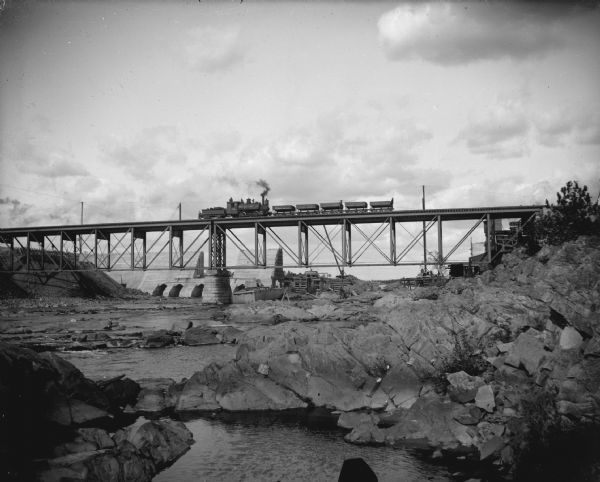 Construction of a dam visible from behind a railroad bridge. A train is crossing the bridge.
