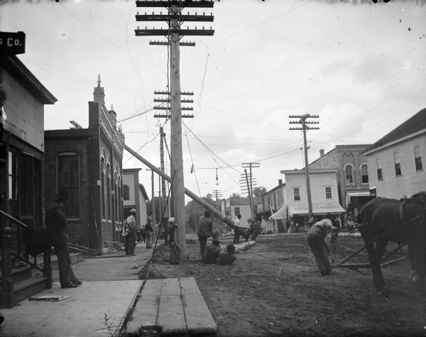 Workmen erecting a telephone pole with a horse team.