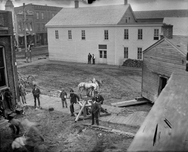 Elevated view of team of horses powering a winch for moving a house at the rear of the Jackson County Bank.