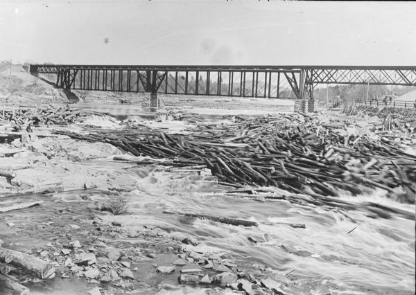 Log jam floating by the first railroad bridge over the river.