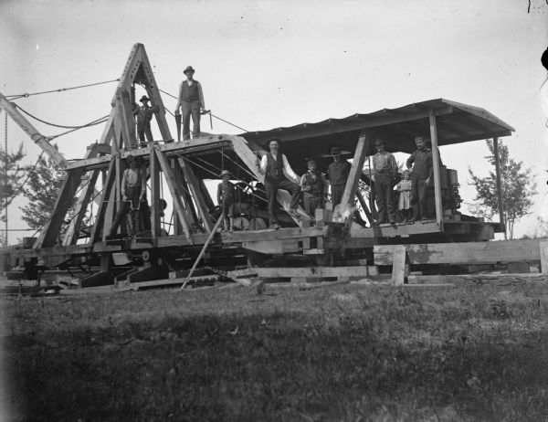 View across grass towards men, boys, and girl posing on top of a walking dredge.