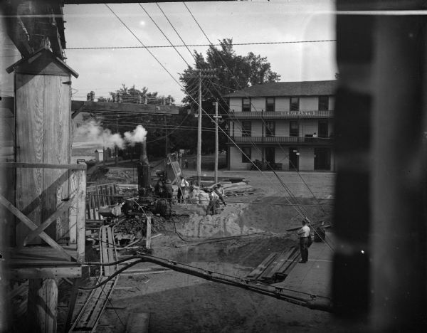 Men constructing a building, or laying a foundation for the post-flood business district dam, using steam-powered machinery in front of the Merchants Hotel.