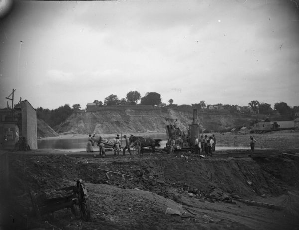 Men constructing the post-flood business district dam using steam-powered machinery.