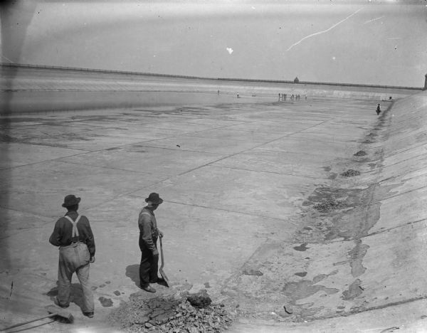 Men working in a drained reservoir with shovels, probably at the Hatfield Dam.