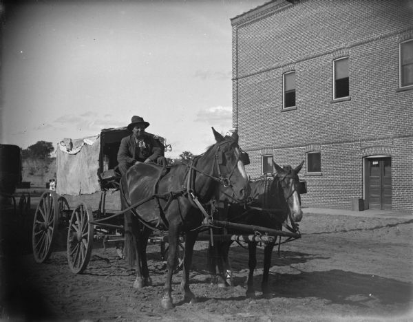 Tall horse and short horse drawing a covered-box wagon, probably the southeast corner of First and Main Streets.