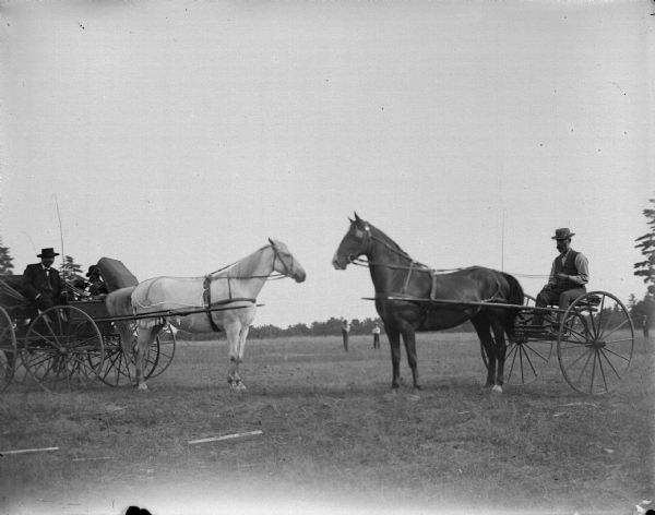 Horse and buggy of a man from town meets the road cart/sulky of the farmer. People are standing in a field in the background.