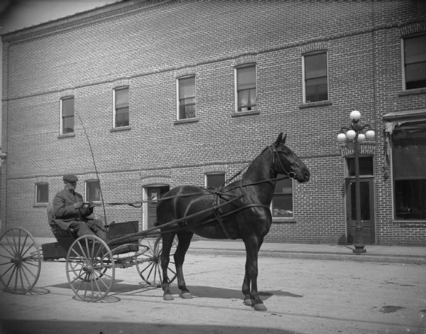 Man in a horse and wagon in town, possibly Henny Berg in front of the Cozy Corner Tavern after the flood of 1911. A large lamppost is on the sidewalk on the other side of the street.