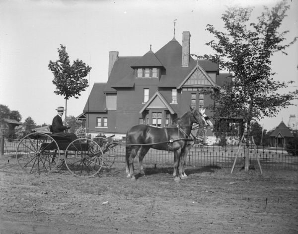 Hugh Price in a top-buggy pulled by a team of two horses posing in front of the home of W.T. Price.