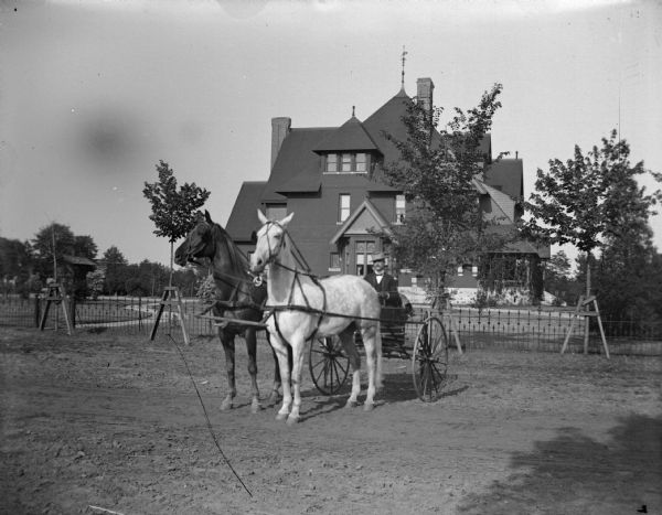 Hugh Price in a top-buggy pulled by a team of two horses posing in front of the home of W.T. Price.