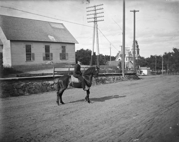 Man riding a horse into town, in front of the old Catholic Church which lost its steeple in a storm.