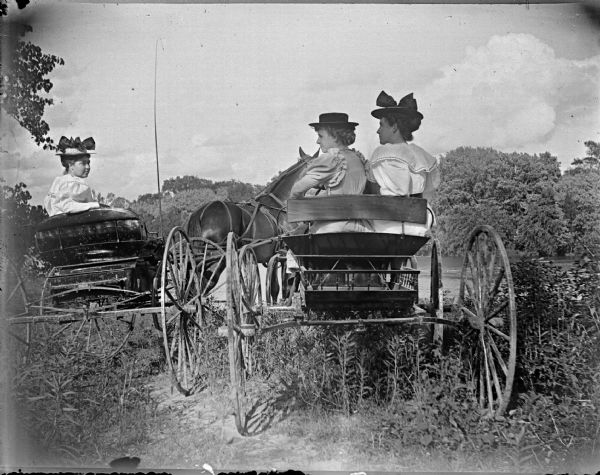 Rear view of three women in two buggies. The Spaulding twins, Mary and Jane, are in one buggy on the right, conversing with Helen Bryant Heald in the other buggy on the left.