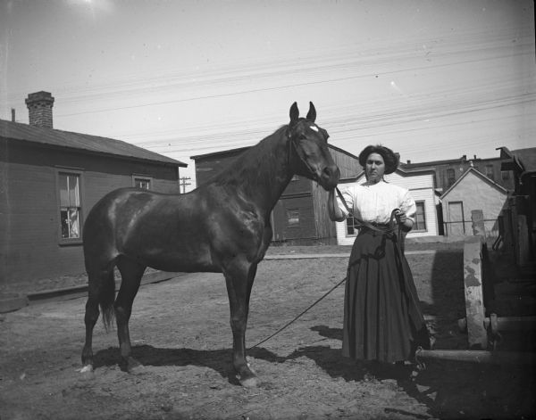 Woman posing with horse with a white-blazed forehead. Buildings are in the background.