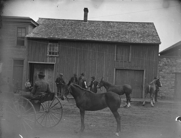 Men displaying horses. The man in the center is probably John Meek. Buildings are along the opposite side of the street.