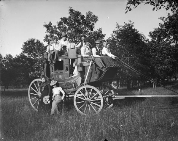 Group posing with a stagecoach known as the "W.T. Price Stagecoach." Beside the lady driver, in the center front seat, is Frank Oberholtz. On the top rear, from left to right, is Alvin Jones and Tip Robie. The ladies below, from left to right, are Lottie Bright and Myra Mason Werner.