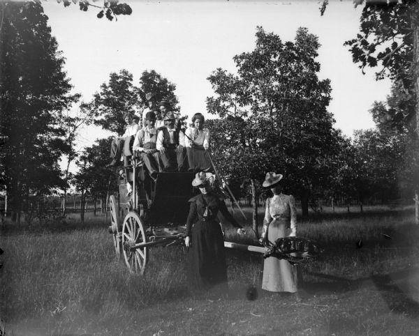 Group posing on stagecoach in field.	
