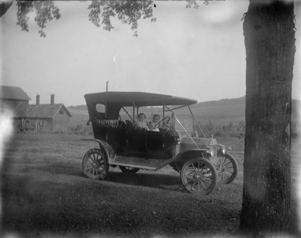 Two girls posed inside an automobile, probably a Model-T Ford.