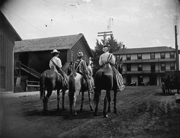 Rear view of three patriotically dressed women on horseback in town, riding toward the Merchant Inn.