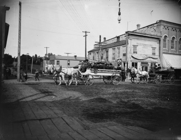 Horse-drawn wagon with band followed by a wagon with an advertisement.