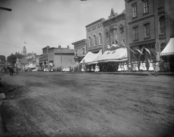 Patriotic parade, probably Memorial Day, through town on the board sidewalk, in front of the First National Bank looking back toward the Jackson County Court House.