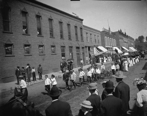 Boys walking in a Memorial Day parade, in front of the Women's Relief Corps with umbrellas.