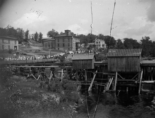 Patriotic parade crossing the bridge into town and probably heading up German Hill. The buildings identified, from right to left, the Spaulding wagon shop, city boarding house for the poor and young, and the Metzger house.