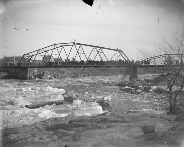 Bridge into town lined with people and icy water below.