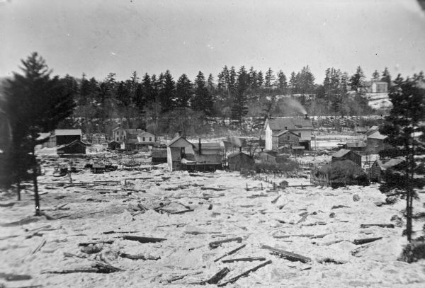 Town with logs overflowing the river into yards, probably the Ice Gorge of 1876.