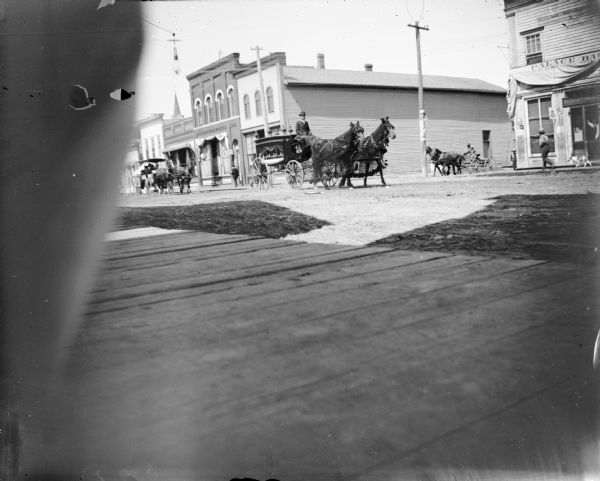 View across board sidewalk towards a hearse being pulled by a team of two horses wearing fly-nets.