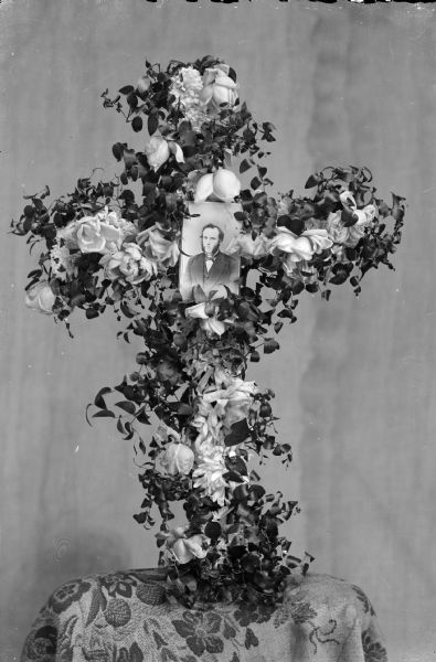 Memorial cross of flowers with a photographic portrait of a man with muttonchops in the middle.