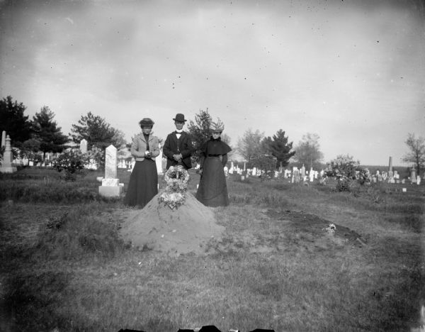 Two women and a man visit a recent grave.