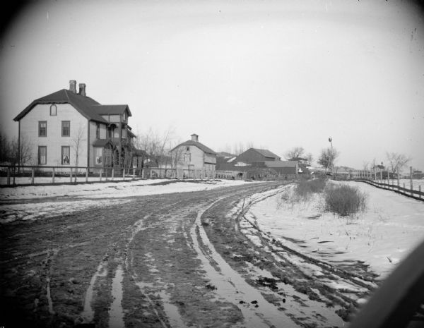 Snowy and muddy road by several farmhouses and farm buildings.