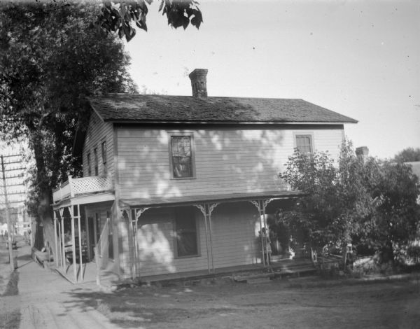 Two-story frame house in town with two porches, and a small girl standing on a porch.