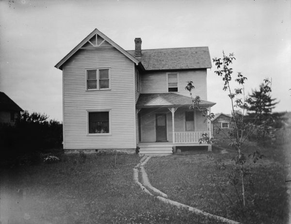 Two-story frame house with a porch on the right half. A log sidewalk is in the front yard.