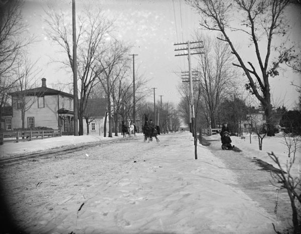 Winter scene with sleds and sleighs on a snow-covered street in Black River Falls, Wisconsin. The man in center sleigh is probably Moses Paquette.