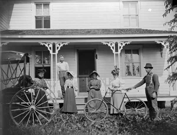 Group of people in front of a frame house. Four women and two men, one holding a bicycle.