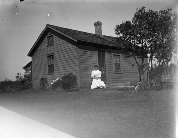 Woman posed sitting in front of a frame house.