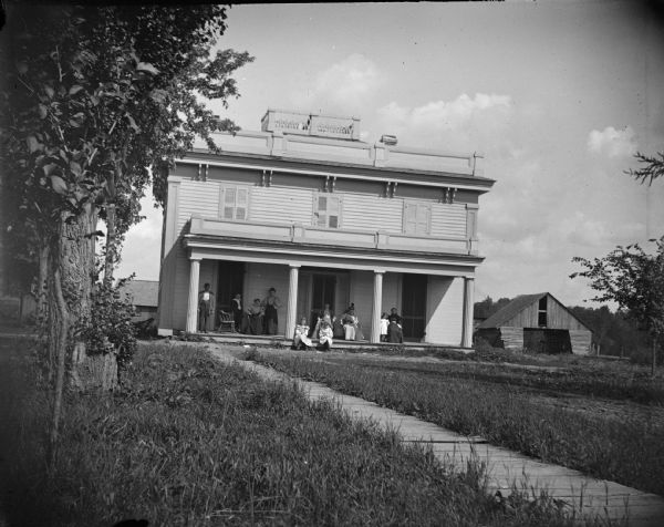 Seven women, man, and boy posing on the porch of a two-story home.