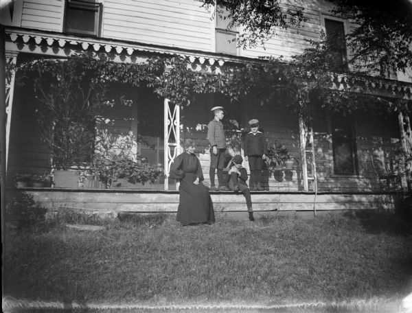 Woman and three boys posing on a long porch with potted plants.