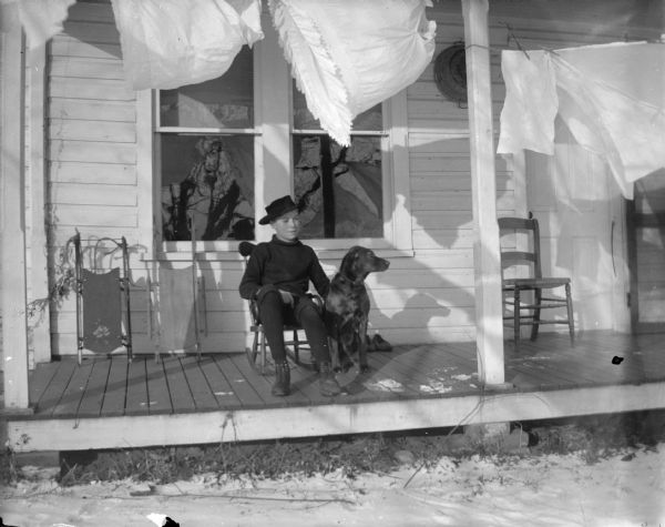 Boy sitting with dog on porch with a clothesline hanging with petticoats.