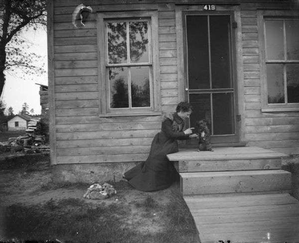 Woman and a begging dog on the steps of a frame house, numbered 419.