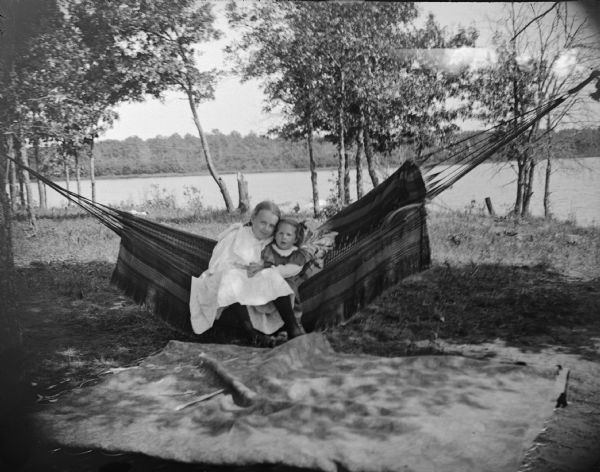 Outdoor view of two girls in a hammock in a backyard. Water is indw
 the background.