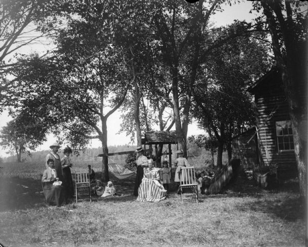 Man, four women, four girls, and two boys in the yard of a house near hammocks.