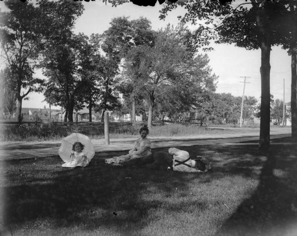 Reclining man, seated woman, and a girl holding an umbrella on a lawn.