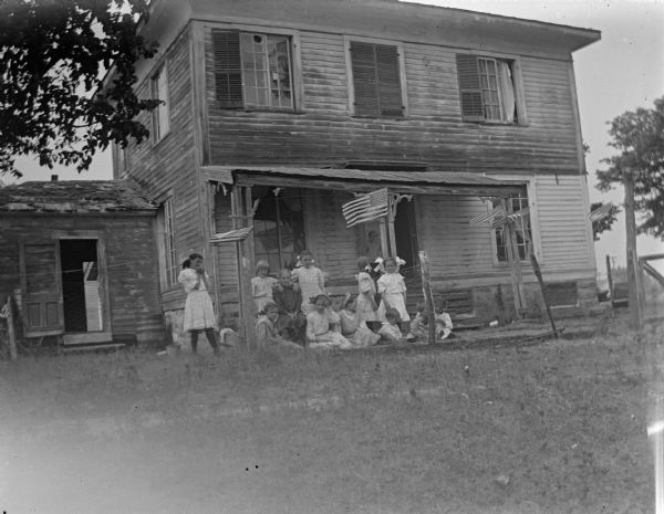 Group of girls posing in the yard of a clapboard house decorated with American flags.