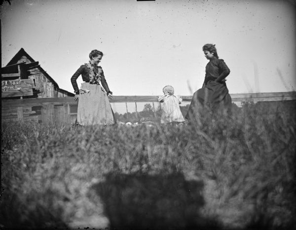 Two women and a girl standing in a field with rabbits.